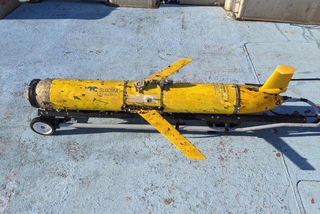 The yellow ocean glider on the deck of a boat, covered in barnacles.