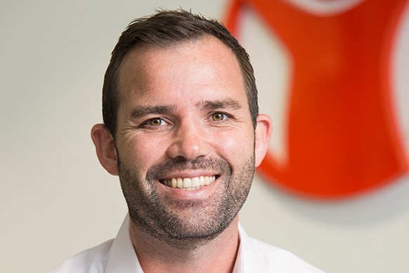 Mat Tinkler, with brown hair and stubble, smiles, wearing white shirt.