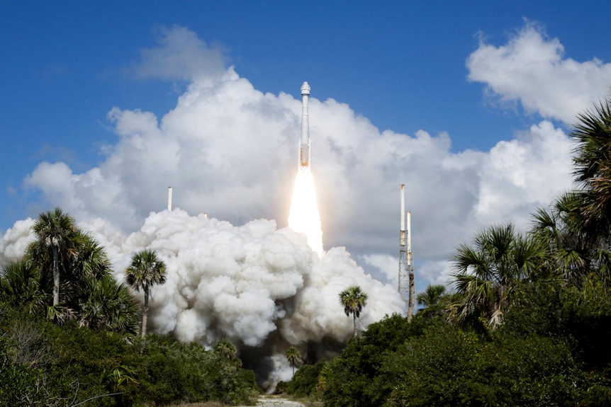 A rocket is launched to space in a big cloud of smoke from a location with palm trees and blue skies