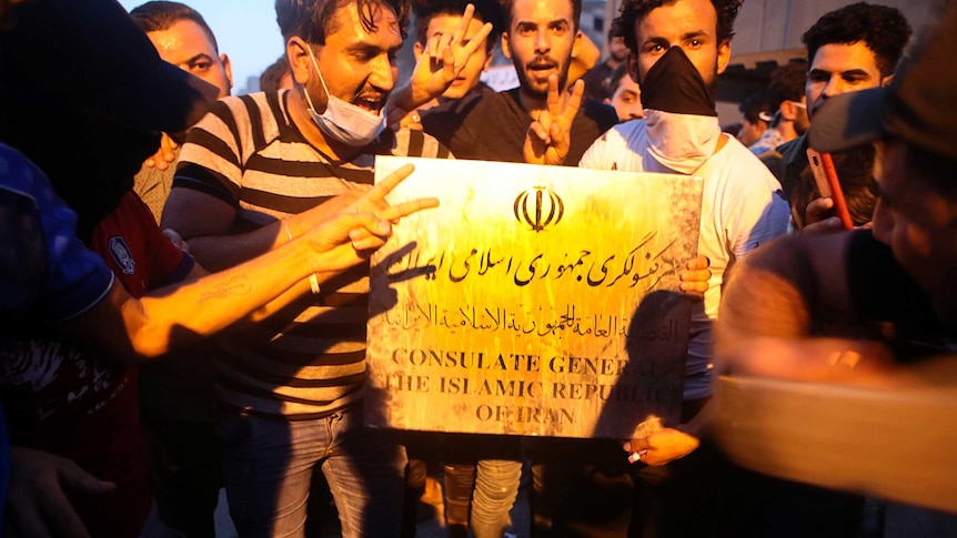 Protesters hold a sign belonging to the Iranian consulate building before storming and burning it