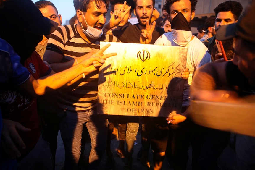 Protesters hold a sign belonging to the Iranian consulate building before storming and burning it