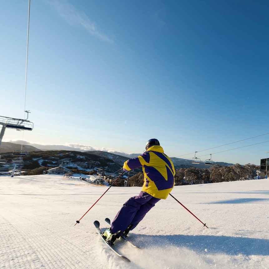 Person in yellow and purple snow gear skiing down snow covered mountain