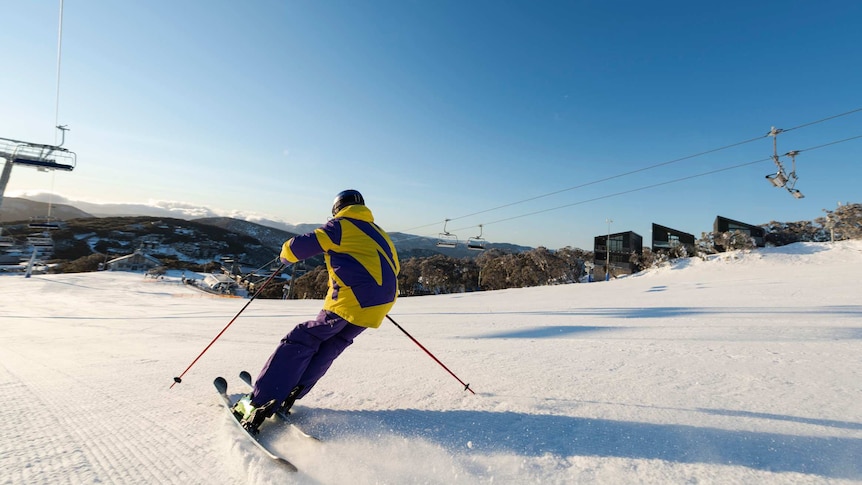 Person in yellow and purple snow gear skiing down snow covered mountain
