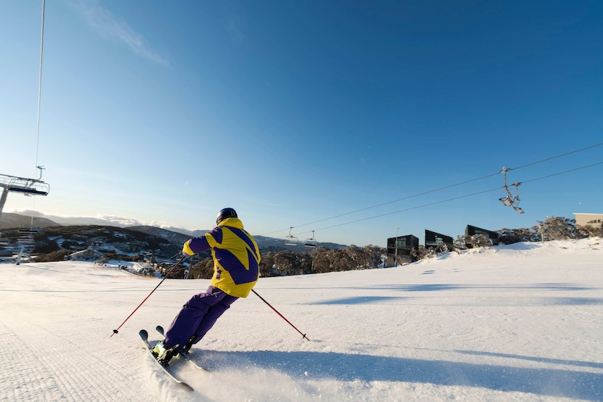 Person in yellow and purple snow gear skiing down snow-covered mountain