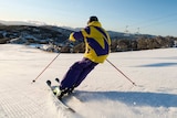 Person in yellow and purple snow gear skiing down snow covered mountain.