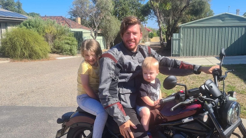 Aaron huddy sitting on a motorbike with his daughter on his left and son on his right