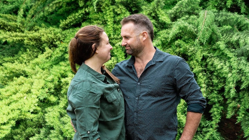 A couple smile at each other while standing outside.