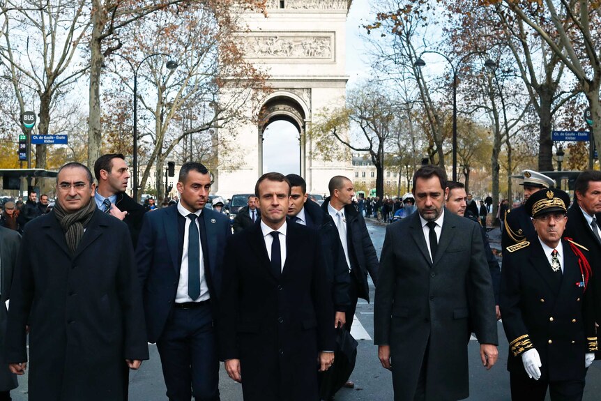 Emmanuel Macron and other men walk down a street near the Arc de Triomphe