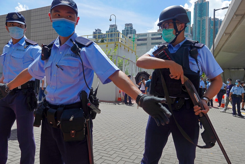 Several police officers wearing protective face masks stand guard as Tong Ying-kit, arrives at a court in Hong Kong.