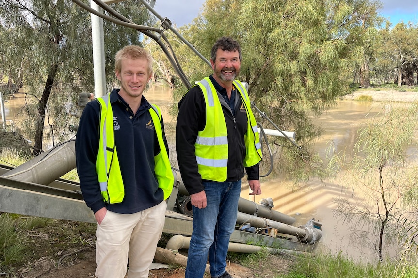 Dylan Klingbiel and Wayne Ellis stand on the bank of the Darling River with the pump and fish screen in the background