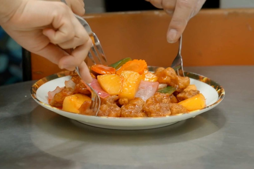 Close up of hands eating sweet and sour pork