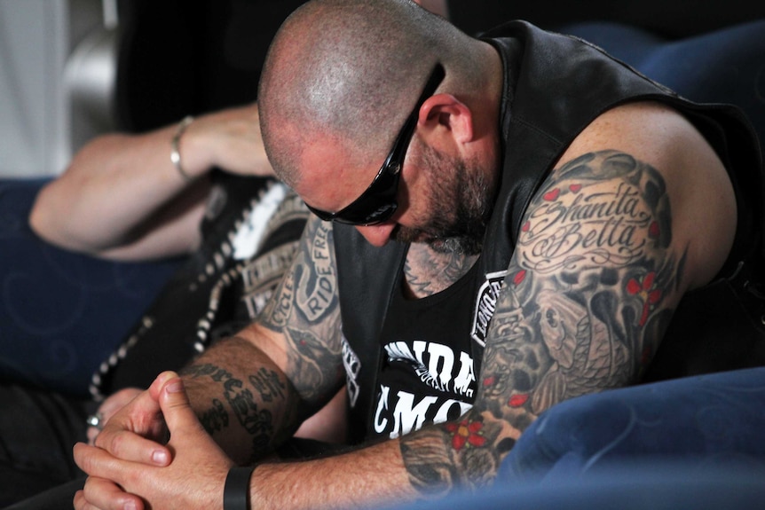 Tattooed man leaning over to pray at the Longriders Church.