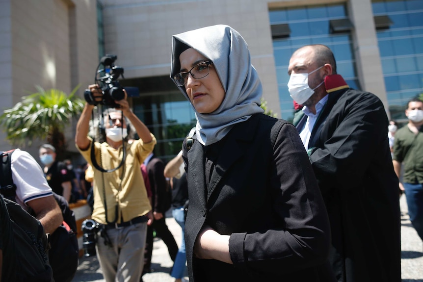 A woman stands in front of a court house surrounded by journalists.