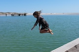 Young girl in a dress leaping off a jetty into the water