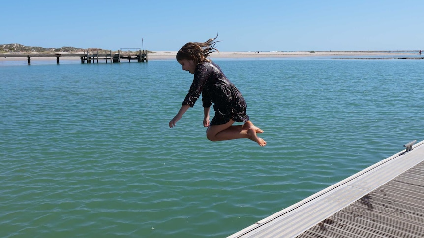 Young girl in a dress leaping off a jetty into the water