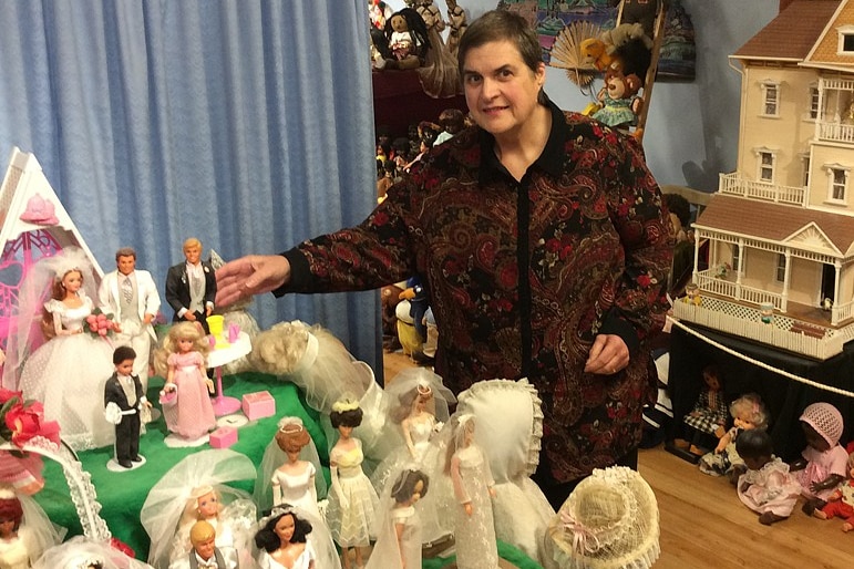 Lady with dark hair on right looking at wedding doll display on left, doll house in background