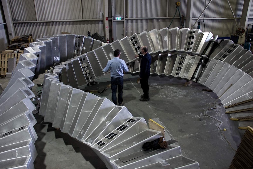 Two men standing in front of a twisting aluminium frame structure.