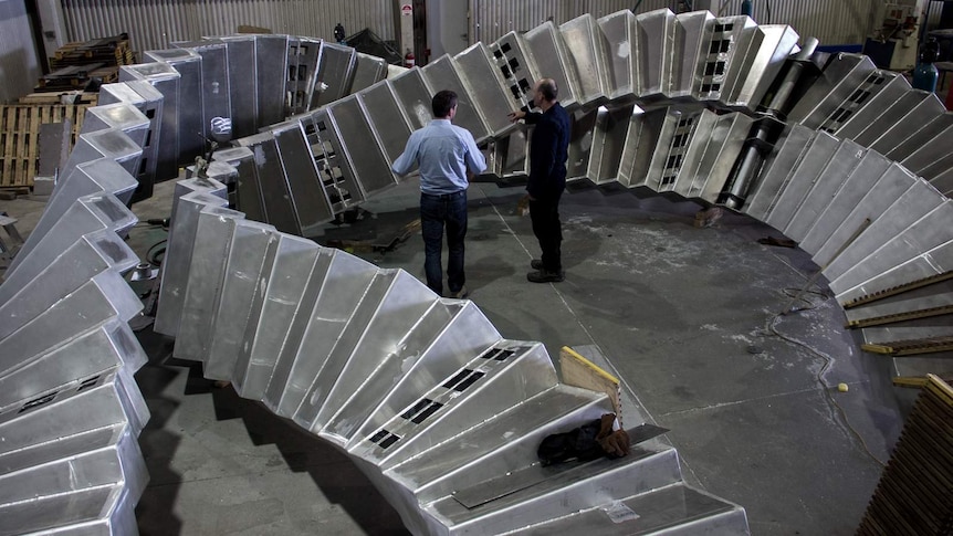 Two men standing in front of a twisting aluminium frame structure.