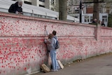Two people write on a wall decorated with red and pink love hearts.