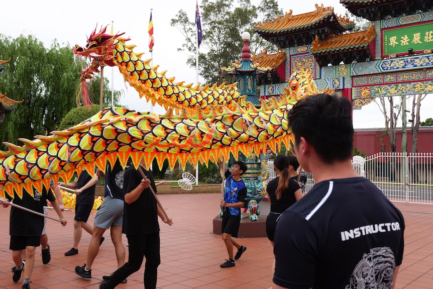 A man watches as a dragon puppet is carried in a circle by a group of teenagers