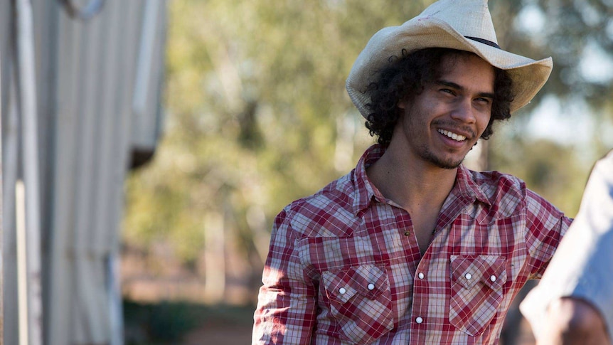 Indigenous actor Mark Coles Smith, wearing a hat and a checked shirt.