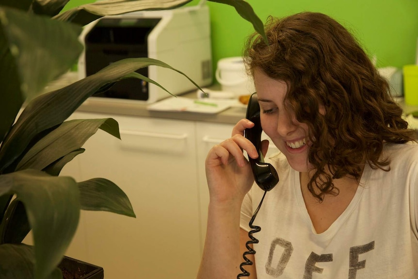 Young woman smiling as she listens on the phone in an office
