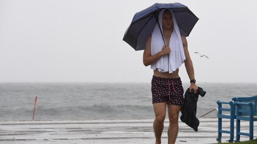 a man in beach gear holding an umbrella at the beach during rain