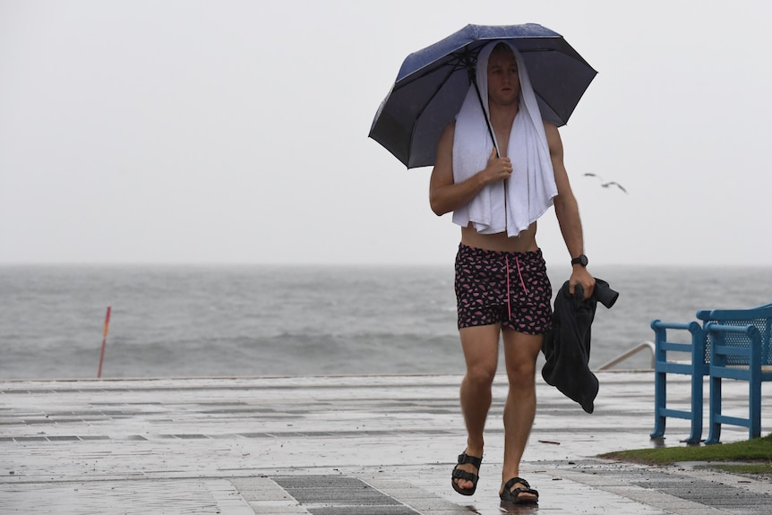 a man in beach gear holding an umbrella at the beach during rain