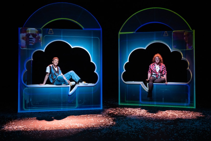 A trans man and a trans woman, dressed as teenagers in the 00s, sit inside speech marks on a stage