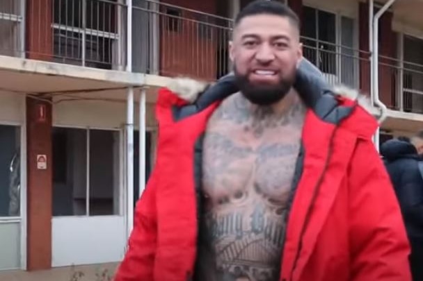 a heavily tattooed man in a jacket with his chest bare