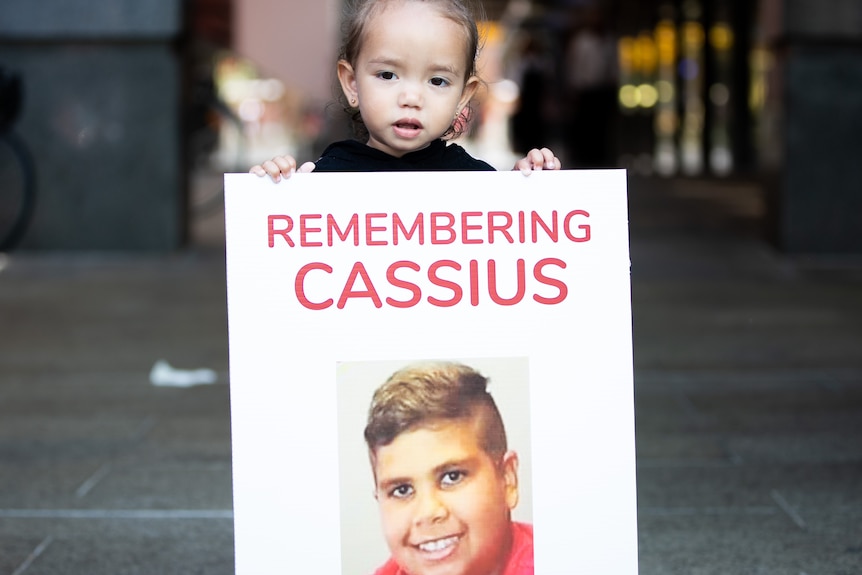 A young girl holding a poster saying 'Remembering Cassius".