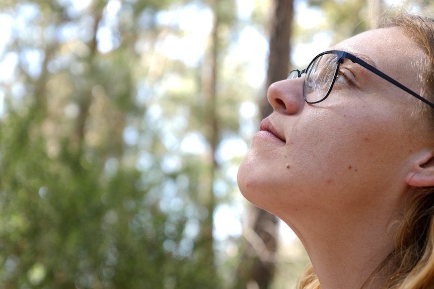 Close-up of a young woman's face as she looks up at the trees thoughtfully
