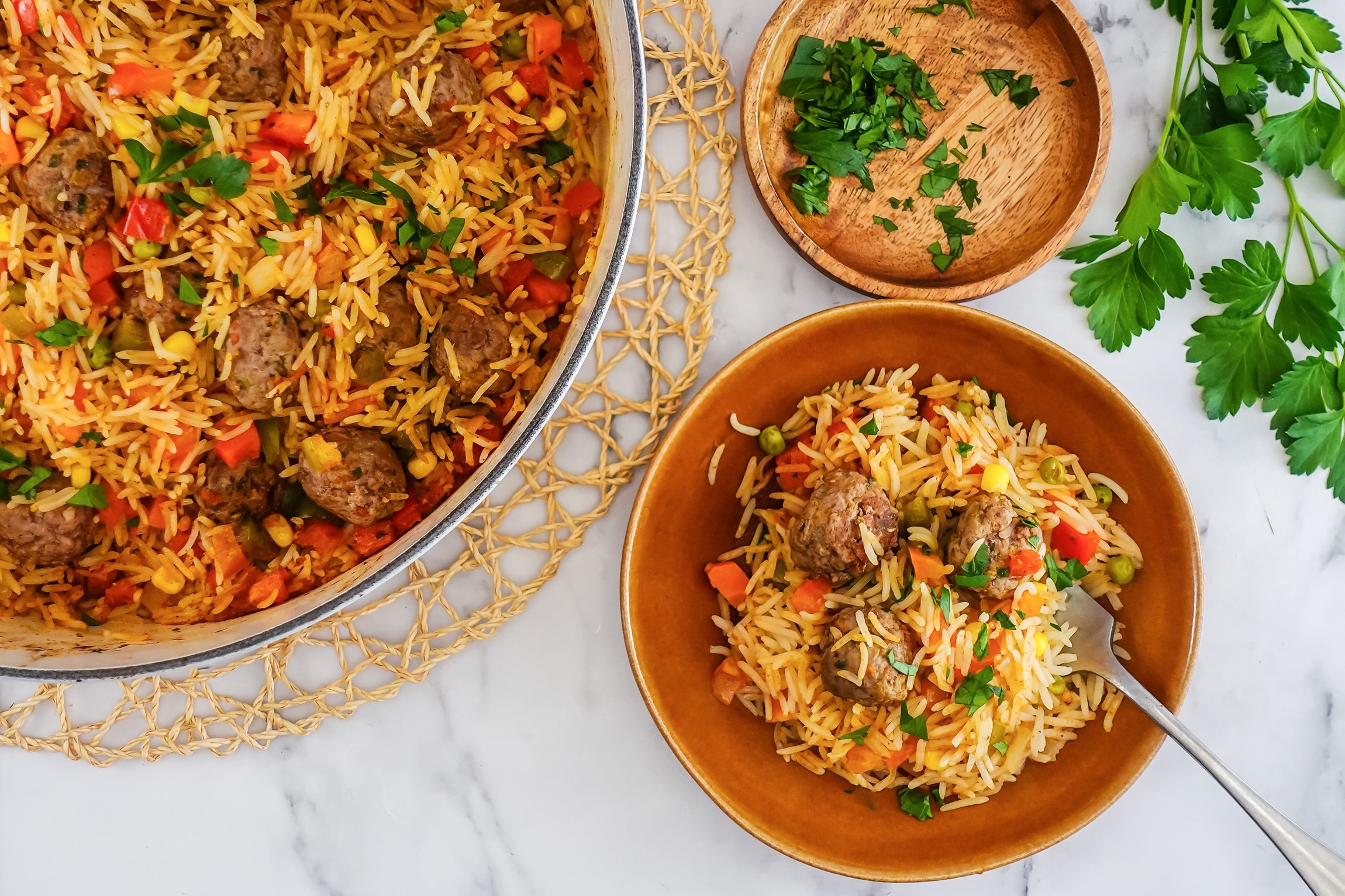 An aerial photo of a small bowl holding rice, mixed veggies like carrot and peas and meatballs. Next to a pot full of the same