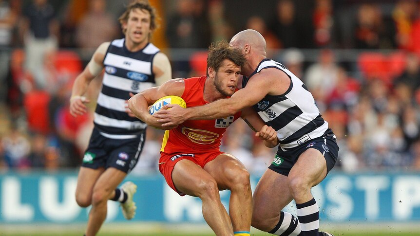 Gold Coast's Maverick Weller and Geelong's Paul Chapman are locked in a tackle at Metricon Stadium.