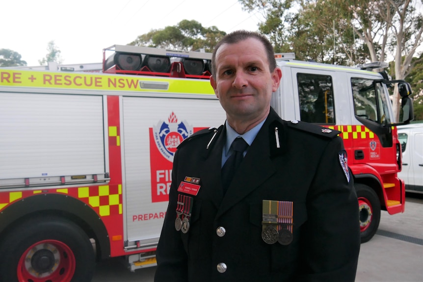 Man in uniform wears FRNSW badges and stand in front of fire truck 