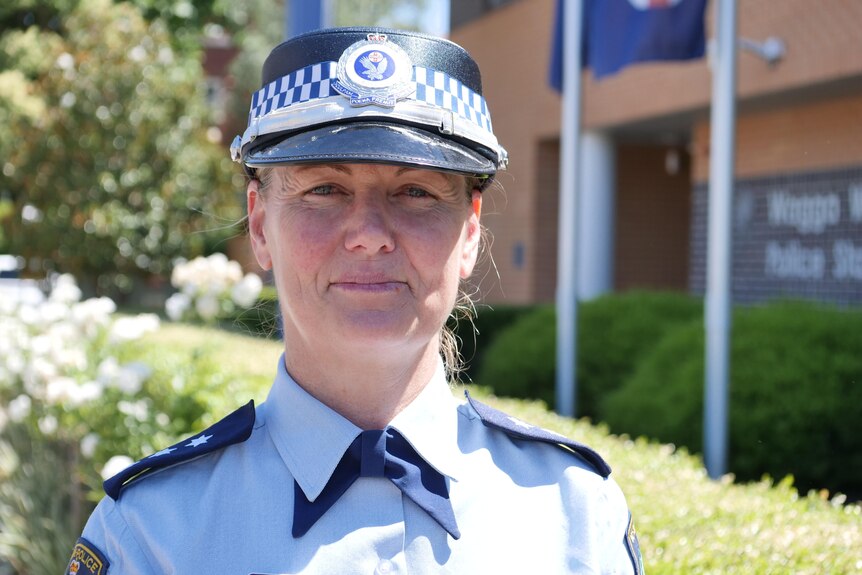 A woman wearing police uniform looks at the camera in front of a police station.