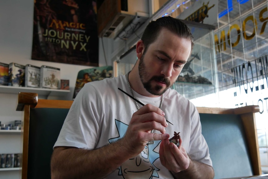A man paints a small figurine with a tiny brush inside a shop.