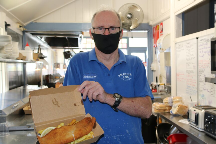 Man in mask holds box of fried fish and chips