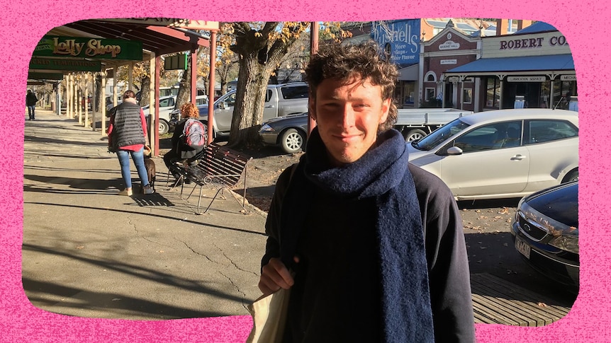 A young man stands in the street smiling.