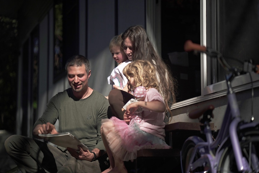 A man and a woman look at a photo album with their two little girls 