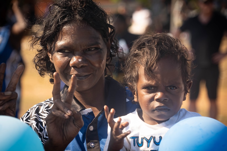 A woman and a child do hand gestures at the camera. They are wearing blue