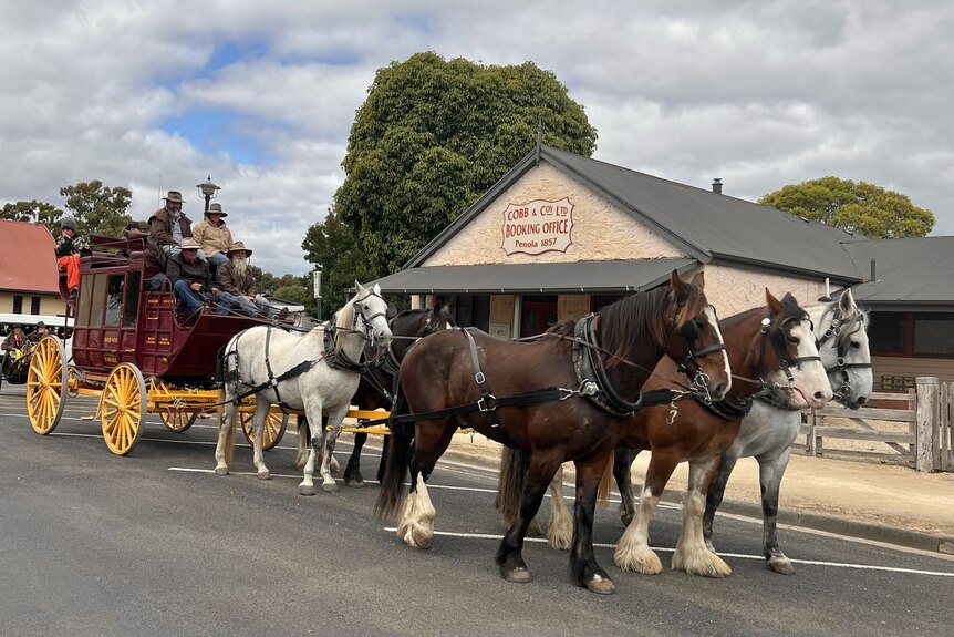 A stagecoach with a team of five horses in front of an historic stone building once used as a mail depot
