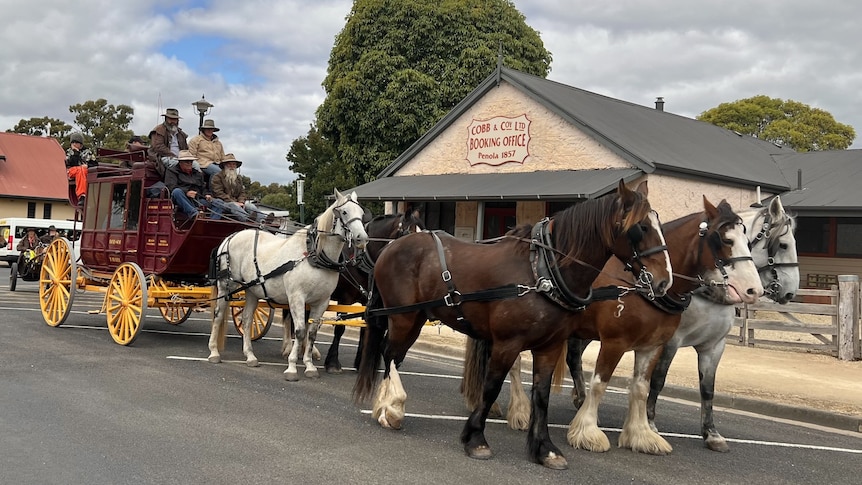A stagecoach with a team of five horses in front of an historic stone building once used as a mail depot