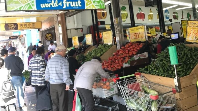 People gather around a the front of a fruit shop and select produce.