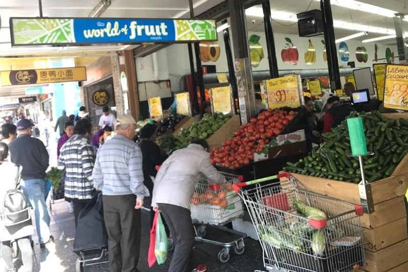 People gather around a the front of a fruit shop and select produce.