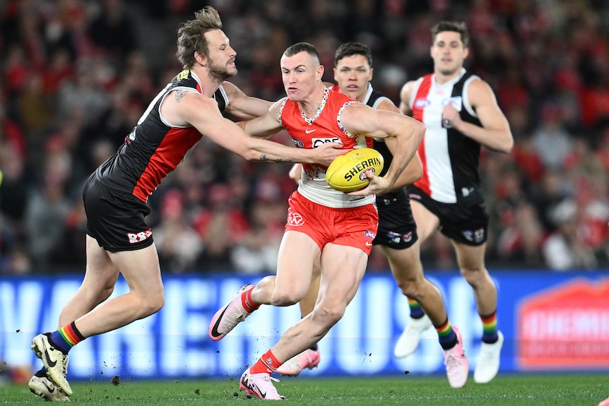 A Sydney Swans AFL player holds the ball as he attempts to palm a St Kilda opponent.