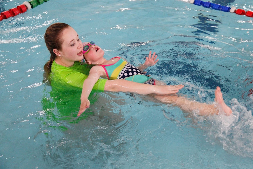 A girl is taught how to swim by an instructor in an indoor pool.