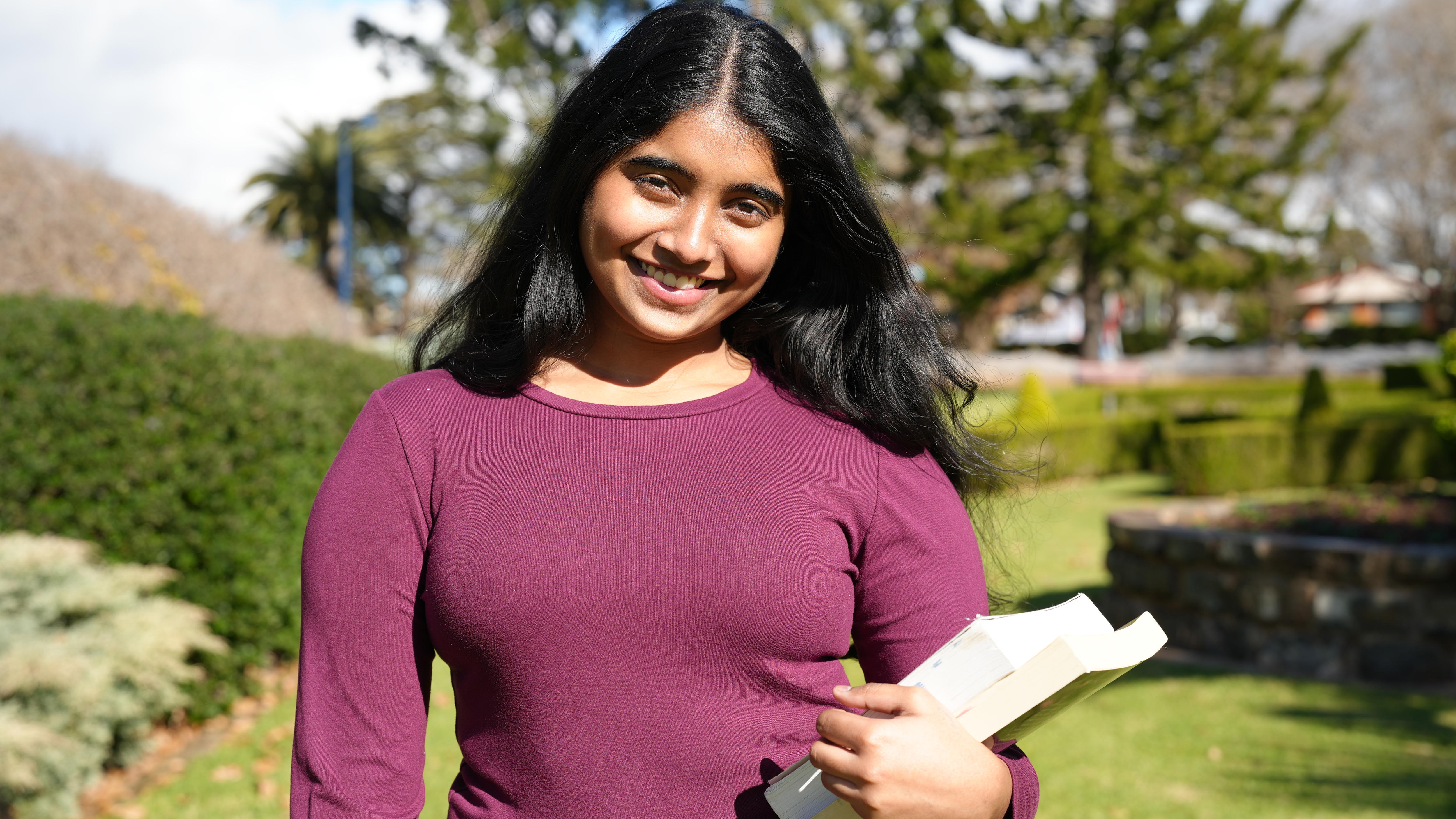 A woman with a black heart wearing a burgundy shirt holds books. 