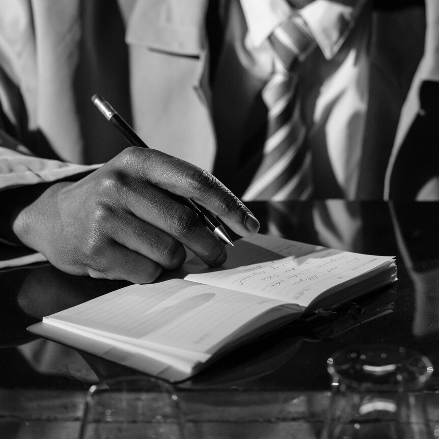 Black and white photo of a man's hand holding a pen over a notebook.