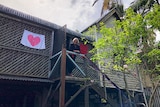 smiling woman standing on a small porch with love heart symbols in house window